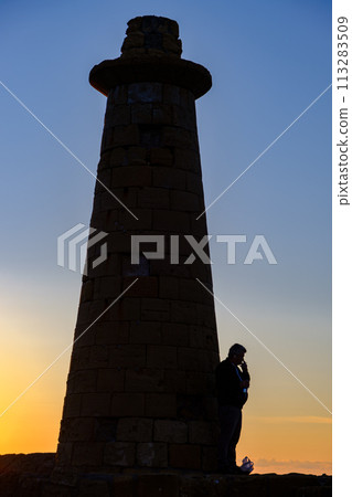 A man standing and smoking by the lighthouse of Kyrenia Harbour at the blue hour in Cyprus 113283509