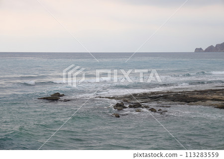 A lone figure in front of foam waves and a historic mountain in Alanya, November 2021. 113283559