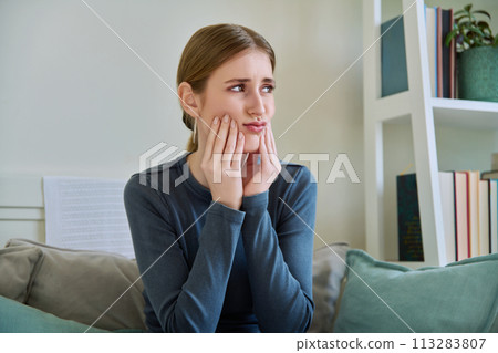 Suffering young teenage female having toothache, sitting on couch at home 113283807