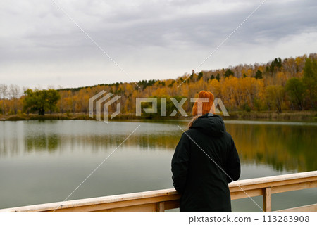 a girl looks at a lake in the autumn forest from a wooden bridge 113283908