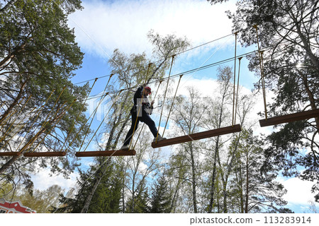 a teenage girl passes an obstacle in a rope park a teenage girl passes an obstacle in a rope park 113283914