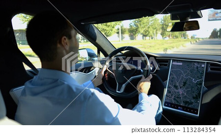 Successful businessman riding on electrical vehicle at city. Male entrepreneur driving a modern electric car at urban road. Businessperson operating auto at sunny day. Young man commuting to work 113284354