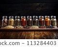 Transparent jars of spices on a wooden table are displayed in a row, on a dark background. 113284403