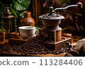 An ancient coffee mill stands on the table, scattered coffee beans, a cup next to it, wooden dishes, greens 113284406
