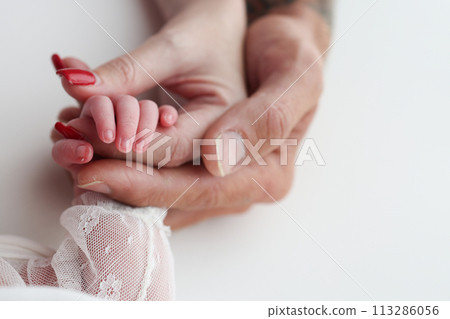 Close-up little hand of child and palm of mother and father. The newborn baby has a firm grip on the parent's finger after birth. A newborn holds on to mom's, dad's finger. 113286056