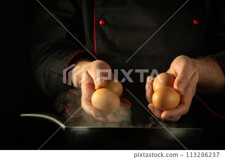 The chef is preparing scrambled eggs in a frying pan. Low key concept of preparing a delicious breakfast in the kitchen of a public house. Grande cuisine The chef is preparing scrambled eggs in a frying pan. Low key concept of preparing a delicious breakfast in the kitchen of a public house. Grande cuisine 113286237
