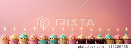 Colorful cupcakes with lit candles are displayed against a pink background, indicating an indoor celebration event marking of joy and celebrating. with free space 113286468