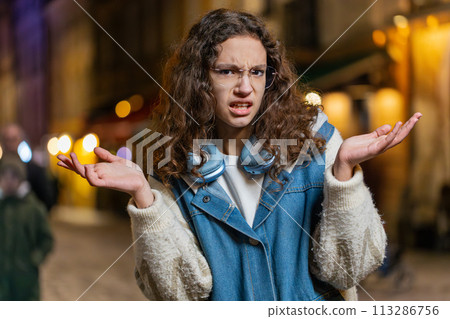 Confused girl feeling embarrassed about ambiguous question having doubts no idea on city street Confused girl feeling embarrassed about ambiguous question having doubts no idea on city street 113286756