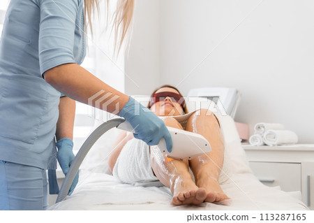 In the beauty clinic, the cosmetologist performs photoepilation on the client's body, ensuring smoothness and beauty of the skin. During the photoepilation procedure, a woman trusts a cosmetology 113287165