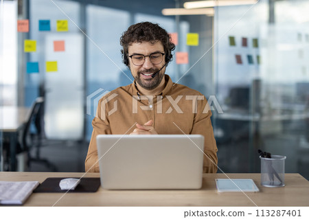 Smiling Hispanic businessman using a headset during a business call in a modern office environment. Professional, engaged, and focused. Smiling Hispanic businessman using a headset during a business call in a modern office environment. Professional, engaged, and focused. 113287401