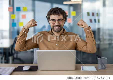 Enthusiastic office worker raising fists in excitement at desk with laptop, expressing triumph. Enthusiastic office worker raising fists in excitement at desk with laptop, expressing triumph. 113287404