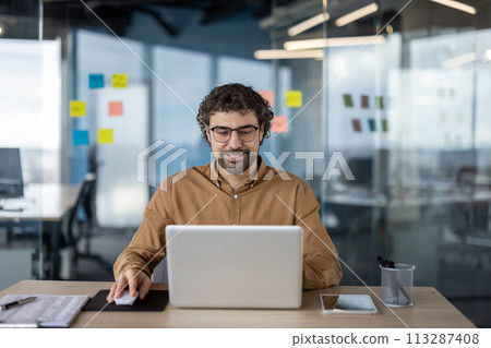 A professional focuses intently on their laptop in a well-lit, contemporary office environment, surrounded by sticky notes and office supplies. 113287408
