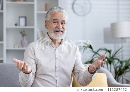 Elderly gentleman comfortably engaged in a video call from his well-lit living room, portraying a casual and relaxed discussion. Elderly gentleman comfortably engaged in a video call from his well-lit living room, portraying a casual and relaxed discussion. 113287452