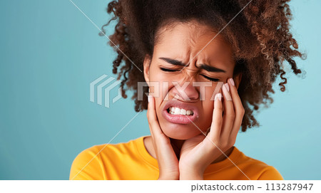 Young black woman holding her cheek with her hand and suffering from severe toothache, blue background. Dental diseases concept, problems with teeth and tooth enamel 113287947