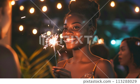 Elegant young African woman in a sparkling dress and a sweet smile celebrates with a sparkler. Portrait of a girl against the background of festive evening garlands Elegant young African woman in a sparkling dress and a sweet smile celebrates with a sparkler. Portrait of a girl against the background of festive evening garlands 113288029