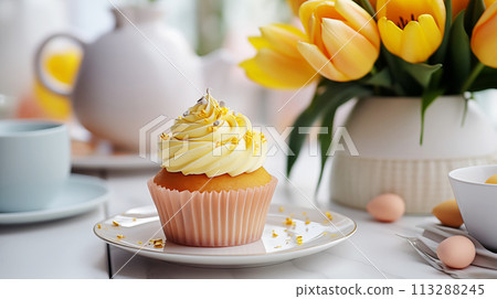 Vanilla cupcakes with creamy filling next to a bouquet of yellow tulips on a festively served table. Spring composition 113288245