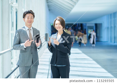 身穿西裝的一男一女手裡拿著便攜式數位通訊設備 身穿西裝的一男一女手裡拿著便攜式數位通訊設備 113293505