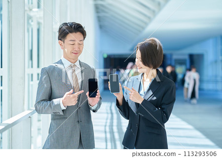 身穿西裝的一男一女手裡拿著便攜式數位通訊設備 身穿西裝的一男一女手裡拿著便攜式數位通訊設備 113293506
