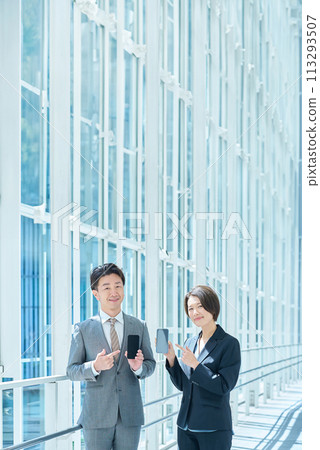 身穿西裝的一男一女手裡拿著便攜式數位通訊設備 身穿西裝的一男一女手裡拿著便攜式數位通訊設備 113293507