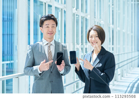 身穿西裝的一男一女手裡拿著便攜式數位通訊設備 身穿西裝的一男一女手裡拿著便攜式數位通訊設備 113293508