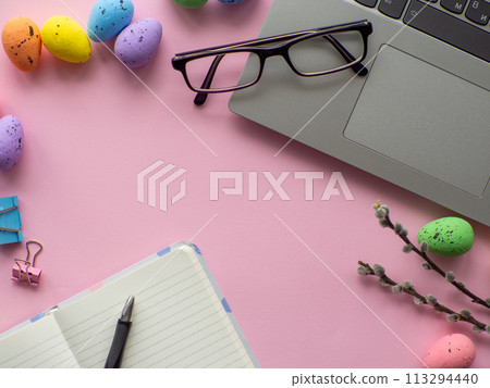 Work desk with devices and easter holiday multicolored eggs on pink background Work desk with devices and easter holiday multicolored eggs on pink background 113294440
