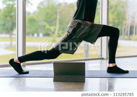 Young Asian man doing online yoga while watching a video on a tablet (crescent moon pose, feet) Young Asian man doing online yoga while watching a video on a tablet (crescent moon pose, feet) 113295785