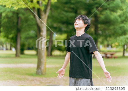 A young man in sportswear taking a deep breath (forest bathing, stress relief, mood change, morning activities, warm-up exercises, sunbathing) 113295805