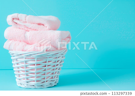 Stack of clean towels in laundry wicker basket on blue background. The towels showcasing their soft and fluffy textures Stack of clean towels in laundry wicker basket on blue background. The towels showcasing their soft and fluffy textures 113297339