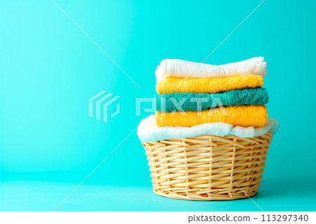 Stack of clean towels in laundry wicker basket on blue background. The towels showcasing their soft and fluffy textures Stack of clean towels in laundry wicker basket on blue background. The towels showcasing their soft and fluffy textures 113297340