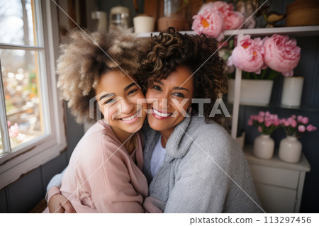 Joyful mother and teenage daughter embracing at home, surrounded by flowers. 113297456