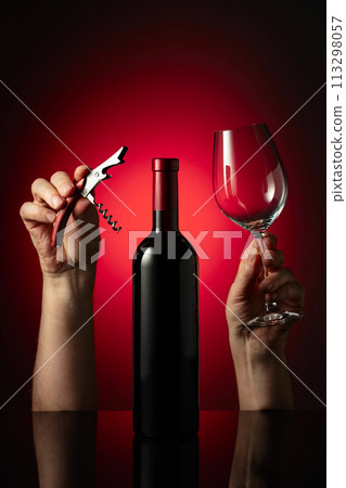 Unopened bottle of red wine and hands with corkscrew and wine glass. 113298057
