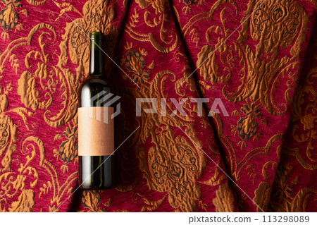 Bottle of red wine on a retro tapestry with dark red and golden floral ornament. 113298089