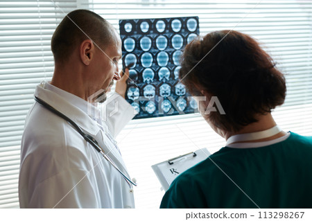 Neurosurgeon examining brain xray of patient when nurse writing down recommendations Neurosurgeon examining brain xray of patient when nurse writing down recommendations 113298267