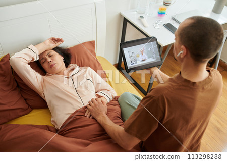 Caring husband holding hand of sick wife when video calling doctor 113298288