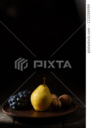 Yellow pear, blue grapes and walnuts in a clay pot on a wooden table Yellow pear, blue grapes and walnuts in a clay pot on a wooden table 113298494