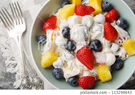 Summer cheesecake salad with strawberries, blueberries, pineapple, dressed with cream cheese and cream close-up in a bowl. Horizontal top view 113298643