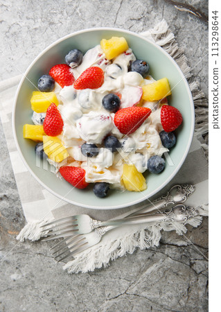 Cheesecake fruit salad with strawberries, blueberries, pineapple close-up in a bowl. Vertical top view 113298644