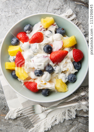 Delicious cheesecake fruit and berry salad with strawberries, blueberries, pineapple close-up in a bowl. Vertical top view 113298645