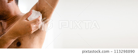 Men apply alum to their armpits to eliminate body odor after they finish showering. Alum helps deodorize men's armpits. The male hand holds alum and rubs the armpit area to eliminate the bad smell. Men apply alum to their armpits to eliminate body odor after they finish showering. Alum helps deodorize men's armpits. The male hand holds alum and rubs the armpit area to eliminate the bad smell. 113298890