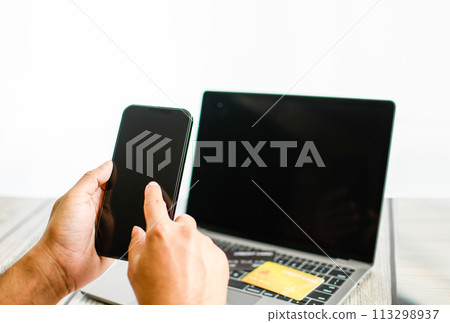 Men use smartphones to shop online. Businessmen transfer money via the Internet. A man's hand holds a smartphone to payment. Business people use laptops on a desk. Selective focus. Blurred background. Men use smartphones to shop online. Businessmen transfer money via the Internet. A man's hand holds a smartphone to payment. Business people use laptops on a desk. Selective focus. Blurred background. 113298937