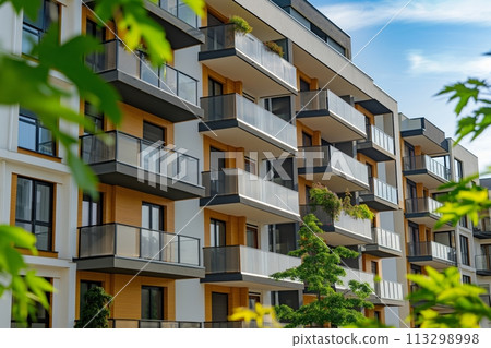 Modern apartment building with vibrant orange facade and protruding glass balconies under a blue sky 113298998