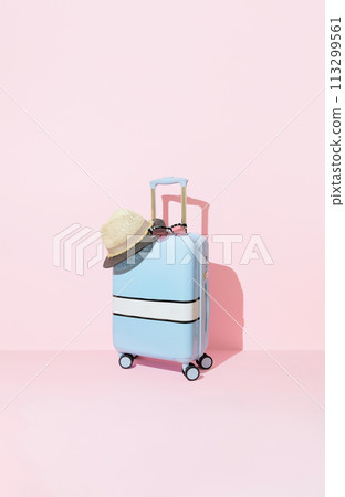 Blue suitcase with sunglasses and hat on a pastel pink background with long deep shadows. Travel concept Blue suitcase with sunglasses and hat on a pastel pink background with long deep shadows. Travel concept 113299561