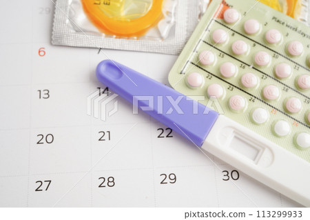 Pregnancy test with birth control pills and condom for female on calendar, ovulation day. 113299933