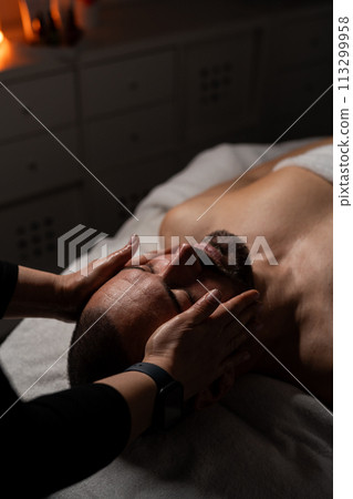 Close up shot of a professional masseuse doing face and head massage for her male client. 113299958