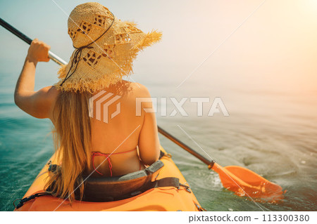 woman straw hat paddling a kayak on a lake. The sun is shining brightly, creating a warm and inviting atmosphere. 113300380