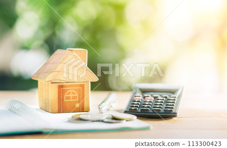 Close up house's model on notebook with calculator, coin and pen on table for Prepare planning of home loan mortgage refinance or retention interest rates, business and financial concept. 113300423