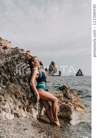 Woman beach vacation photo. A happy tourist in a blue bikini enjoying the scenic view of the sea and volcanic mountains while taking pictures to capture the memories of her travel adventure. Woman beach vacation photo. A happy tourist in a blue bikini enjoying the scenic view of the sea and volcanic mountains while taking pictures to capture the memories of her travel adventure. 113300430