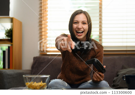 Cheerful caucasian woman with wireless gamepad having fun playing video game at home 113300600