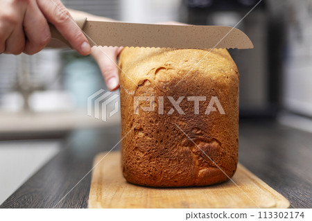Hand slicing freshly baked bread with a bread knife Hand slicing freshly baked bread with a bread knife 113302174