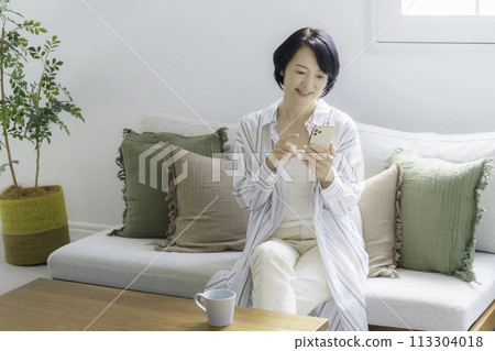 中年婦女坐在客廳的沙發上，看著她的智慧型手機 113304018